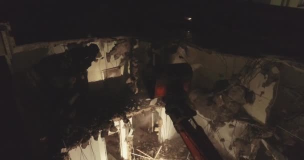 Buldozer de excavator și lopată cu tăietor mare distruge fațada clădirii în mijlocul zonei rezidențiale înconjurată de clădiri de apartamente pe timp de noapte . — Videoclip de stoc