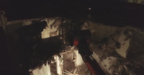 Excavadora bulldozer y pala con gran cortador destruye fachada del edificio en el centro de la zona residencial rodeada de edificios de apartamentos por la noche . — Vídeo de stock