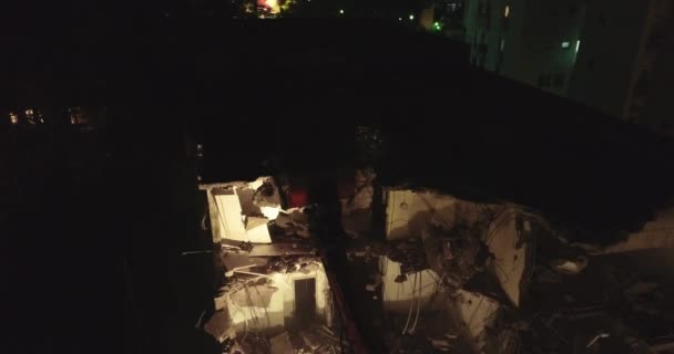 Grävmaskin bulldozer och spade med stor cutter förstör byggnad fasad i mitten av bostadsområdet omgiven av lägenheter byggnader på natten. — Stockvideo