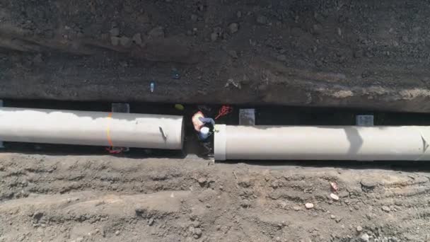 Instalação de tubo de concreto. Aerial acima dos homens no trabalho fora com máquinas pesadas para conectar e instalar água ou tubulação de esgoto em uma terra de solo escavação — Vídeo de Stock