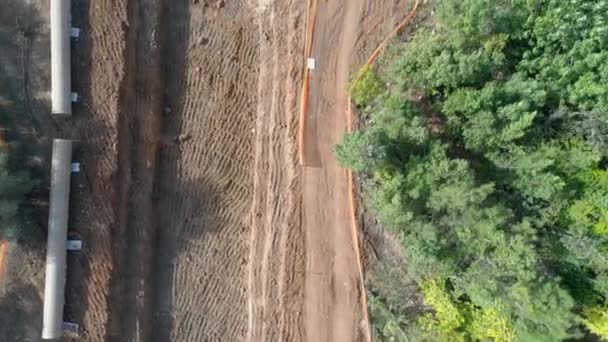 Vliegtuig drone boven bouwplaats buiten bij de natuur met groene bomen rond. Aannemer graven met kraan en schop een waterkanaal plaatsen en installeren van cementpijpleidingen buizen — Stockvideo