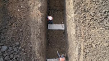 Dışarıda çalışan adamlar ellerinde ağır makinelerle su borularını yüklüyorlar. Kazı araçları, buldozer ya da traktör kazıları ve toprak temizleme arazileri üzerinde.. 