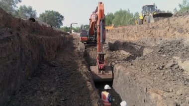 Ulusal altyapı sistemine su boru hattı döşemek için kum zemini kazan turuncu ya da kırmızı kazıcı traktörünün hava görüntüsü. Açık hava inşaat işyeri projesi