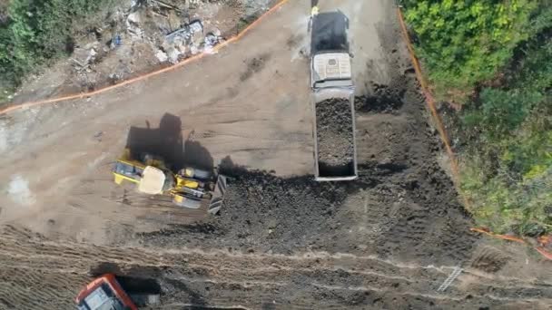 Loading dirt, debris and junk on truck container. Aerial shot above excavator tractor load construction site waste on truck for dumping. heavy machinery industry equipment transportation — Stock Video