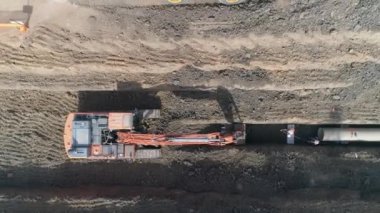 Buldozer, traktör kazısı ve toprak temizleme arazisi üzerinde insansız hava aracı. Dışarıda çalışan adamlar ellerinde ağır makinelerle su borularını yüklüyorlar.