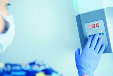 Sağlık görevlisi mikroplara karşı odayı dezenfekte etmek için lambayı yakar. Gösterge panelindeki düğmelere basar, mavi koruyucu bir eldiven verir.                 