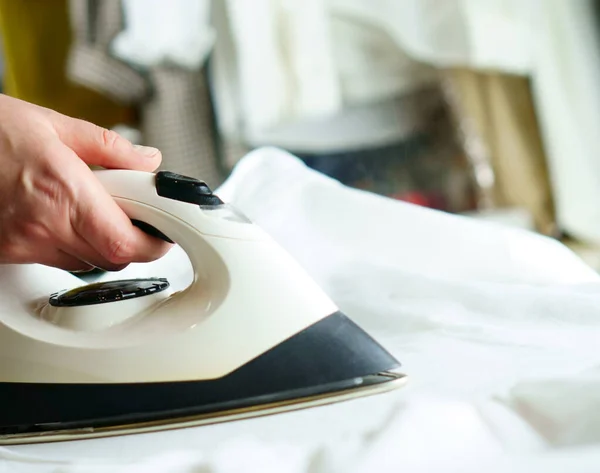 Woman ironing white clothes with a white iron: at home, in the laundry
