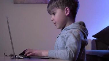 Çocuk video oyunu oynuyor ve bilgisayar kullanıyor. Çocuk bilgisayar ekranına odaklanmış durumda. Geleceğin rgb arka ışıkları