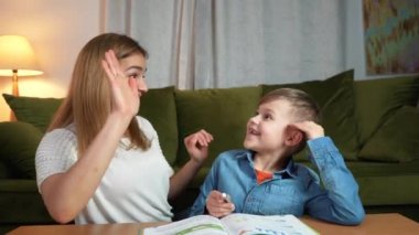 Çekici anne ve oğul evde birlikte çalışıyorlar. Mutlu ve çak bir beşlik. Evde eğitim kavramı. Dadı evde bir çocuğa ev ödevi öğretiyor..