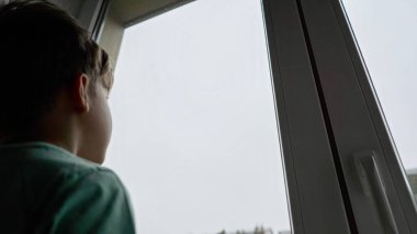 Yalnız çocuk pencereden içeri bakıyor. Sıkıcı çocuk yağmurlu bir günde üzgün hissediyor. Umarım evden dışarı bakıyordur..