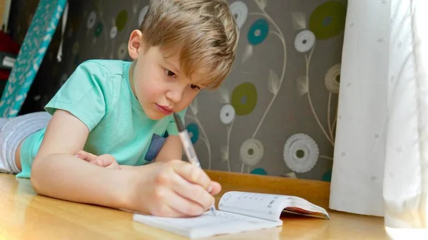 Çocuk konsantre oluyor ve düşünüyor. Çocuk ödevlerini yapıyor ve defterine yazı yazıyor. Matematik yapıyorum..