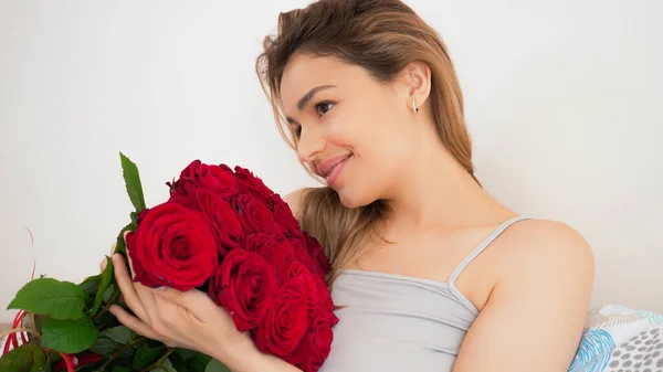 红玫瑰花束的漂亮女人 性感迷人的女性在床上笑着欣赏着家中的花朵 浪漫和女性的概念 漂亮的肖像画 — 图库照片