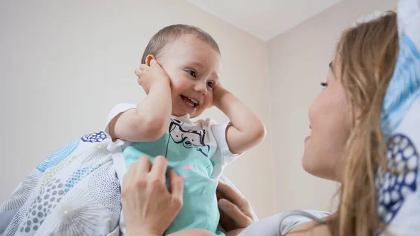 Güzel, genç bir anne ve küçük bir çocuk sabah birlikte eğleniyorlar. Gülümsüyor, gülüyor ve çocukla yatakta oynuyor. Aile mutluluğu konsepti. Parlak, güneşli sıcak bir gün..