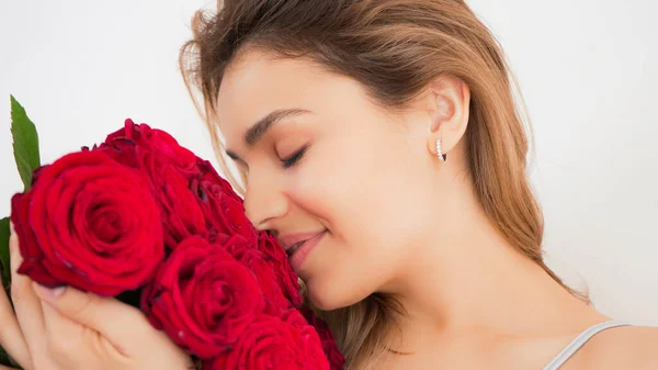 Kırmızı gül buketi olan güzel bir kadın. Şehvetli ve çekici bir kadın gülümseyerek evde çiçeklerin tadını çıkarıyor. Romantik ve kadınsı bir kavram. Yakışıklı portre fotoğrafı..