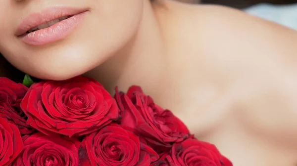 Kırmızı gül buketi olan güzel bir kadın. Şehvetli ve çekici bir kadın gülümseyerek evde çiçeklerin tadını çıkarıyor. Romantik ve kadınsı bir kavram. Yakışıklı portre fotoğrafı..