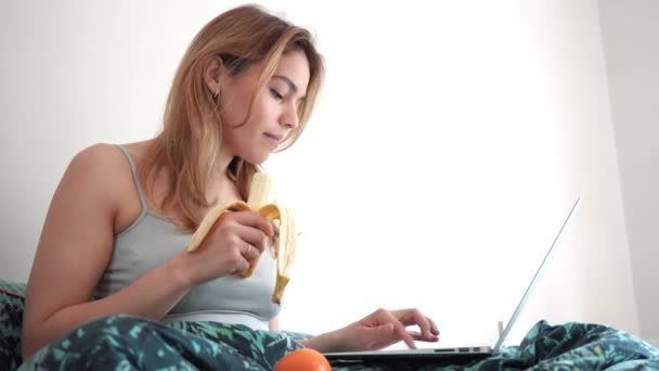 Bella Divertente Giovane Donna Utilizzando Dispositivo Portatile Letto Mangiare Frutta — Video Stock