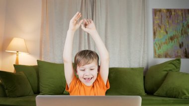 Sevimli çocuk bilgisayar kullanırken tezahürat yapıyor. Mutlu çocuk evde ders çalışıyor. Ev eğitimi kavramı. 