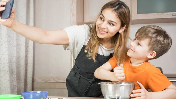 Güzel anne ve oğul evde yemek pişiriyor ve selfie çekiyorlar. Mutlu aile görüntülü görüşme yapıyor. Birlik, bağlantı, ev eğitimi kavramı.