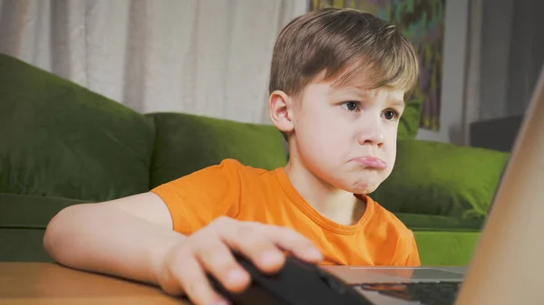 Sad boy using a computer. He feels disappointed studying at home. Home education concept.