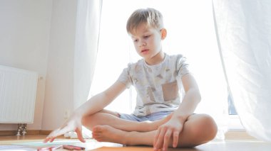 Güneşli bir günde evde oturup ders çalışan tatlı bir çocuk. Ev eğitimi kavramı.