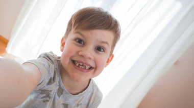 Komik küçük çocuk selfie çekiyor ve yüzünü buruşturuyor. Gülümseyen tatlı çocuk fotoğraf çekiyor ve sohbet ediyor.. 