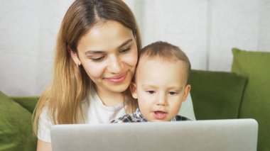 Güzel anne, küçük oğluyla evden çalışıyor. Bağımsız mutlu anne ve çocuk bilgisayar başında çalışıyor. Anne ve bebek görüntülü görüşme yapıyorlar..