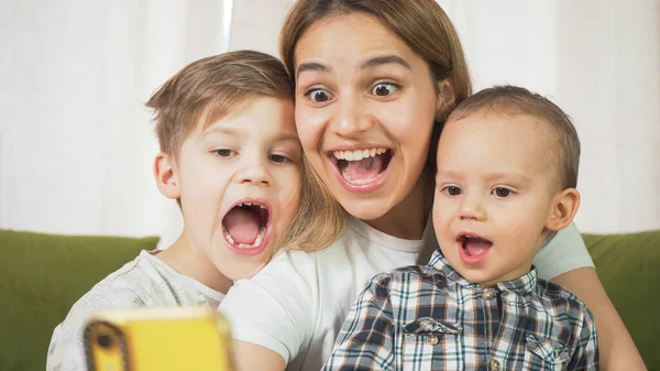 Beautiful mom with sons having a facetime video call. Happy family taking selfies and video chatting at home. Mother's day, unity, connection concept.