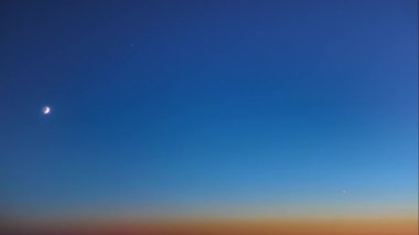 Günbatımından sonraki alacakaranlıkta hilal ayının ve yıldızın karanlık mavi gökyüzünde ufka doğru inişi panoramik bir zaman kayması.