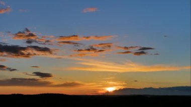 Ufukta bir yaz ormanı üzerinde akan bulutlarla birlikte mavi gökyüzünde turuncu ve sarı tonlarda destansı, pitoresk ve renkli bir günbatımının havadaki panoramik zaman atlaması. 4K 'daki tepeden bak.