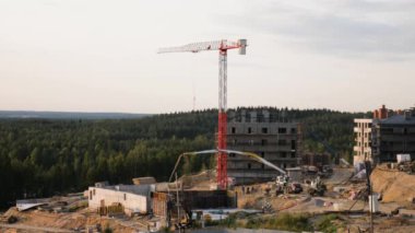 Beyaz kule vinci, kamyon vinci, beton karıştırıcı, yeşil vadi ve ağaçlarda beton kamyonet ve traktör olan banliyö evlerinin inşaat alanlarının panoramik zaman geçişi.