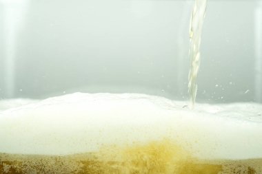 Close up of cool lager beer splash isolated on white background with realistic bubbles & froth in glass. Pouring golden craft beer on front view wave curve shape texture foam for pub & bar menu design
