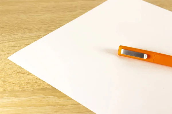 Blank sheet of paper and pen on bright wooden office desk. Ballpoint pen lying on sheet of paper, copy space.