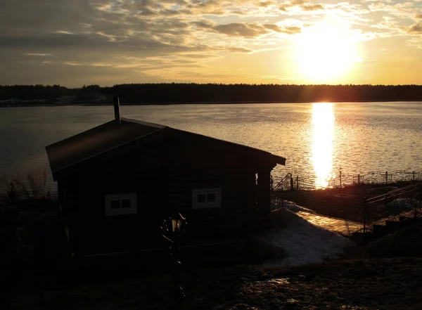 Wooden house on the river. Sunset, spring. House on the river with sunset view. Evening sunrise on a choppy river wind early spring landscape. Sunset in the river with reflex