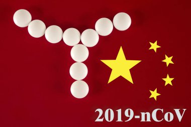 Beyaz tabletlerden yapılmış bir bakteri hücresi. Üzerinde 2019 yazılıydı. Çin bayrağının kırmızı arka planında, üst görünümde. 2019 Roman Coronavirus 2019-ncov konsepti.