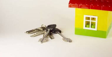 Real estate concept. Small toy house with keys on grey background. With copy space. Selective focus of toy house and keys.