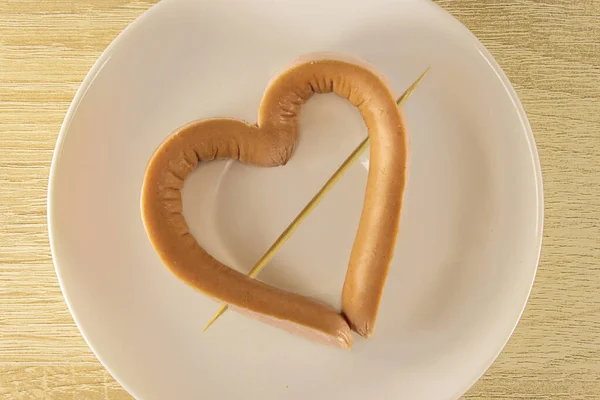 Romantyczne śniadanie w Walentynki: kiełbasa w kształcie serca, przekłuta wykałaczką na talerzu. Jak zrobić pyszne i kreatywne kiełbasy.Fast food Walentynki. — Zdjęcie stockowe