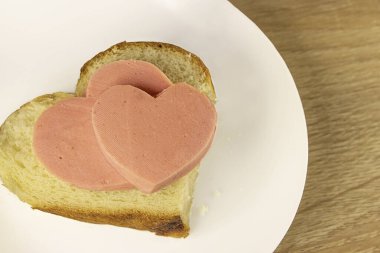 Sevgililer Günü 'nde romantik kahvaltı ahşap arka planda kalp şeklinde jambonlu ekmek sandviçi Sevgililer Günü menüsü. Sosis kalbi. Fast food Sevgililer Günü