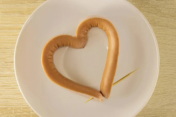 Romantyczne śniadanie w Walentynki: kiełbasa w kształcie serca, przekłuta wykałaczką na talerzu. Menu na Walentynki. Serce kiełbaski. Fast food Walentynki. — Zdjęcie stockowe