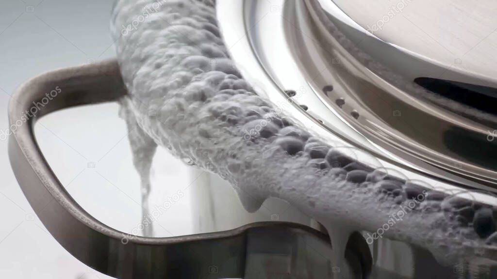 Water boiling over from a saucepan with lid. Pot boiling over. close up