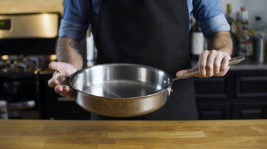 Şefin elleri basit, yeni, paslanmaz çelik tavayı mutfakta tutuyor..