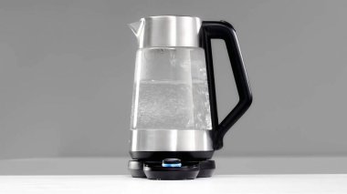 Su bardakta kaynıyor elektrikli su ısıtıcısı. Gri arkaplanda elektrikli su ısıtıcısı