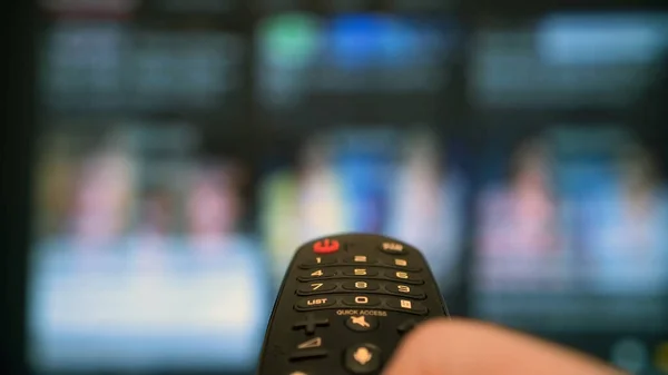 Uzaktan kumanda elinde. Uzaktan kumandayla TV kanalları değiştiriliyor.