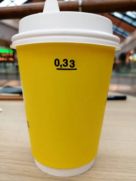 背景がぼやけている白いプラスチック製の蓋付きの黄色い紙のカップ — ストック写真
