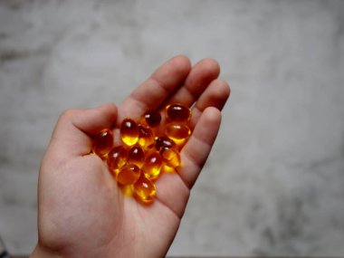 Elinde balık yağı-omega-3 dolu sarı jelatin kapsüllerin tasarımı.