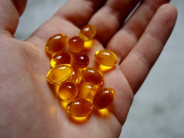 Elinde balık yağı-omega-3 dolu sarı jelatin kapsüllerin tasarımı.