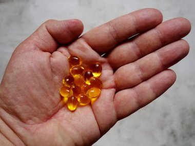 Elinde balık yağı-omega-3 dolu sarı jelatin kapsüllerin tasarımı.