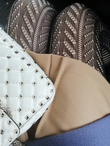 a fashionable composition of a white lady's purse, a beige cashmere  skirt and fishnet tights worn by a young woman