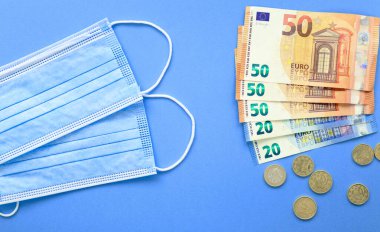 Mascarillas y billetes de euro ayık fondo azul. Compra de mascarillas. Euro. Se dispara el precio de las mascarillas.
