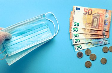 Mascarillas y billetes de euro ayık fondo azul. Compra de mascarillas. Euro. Se dispara el precio de las mascarillas.