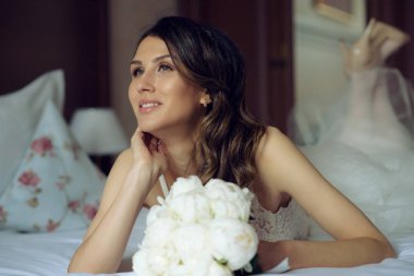 Beyaz şakayıklı genç ve güzel bir gelinin portresi. Yatakta yatıp damadı bekliyor..